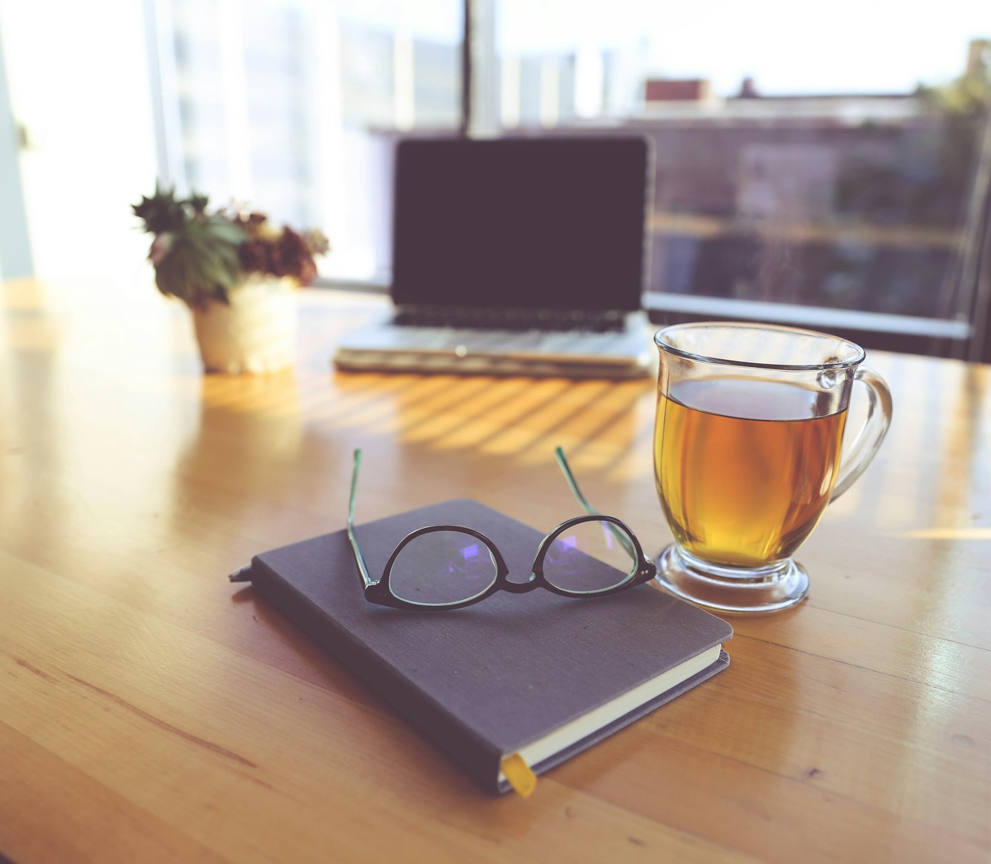 Notebook and glasses on a wooden desk next to tea.