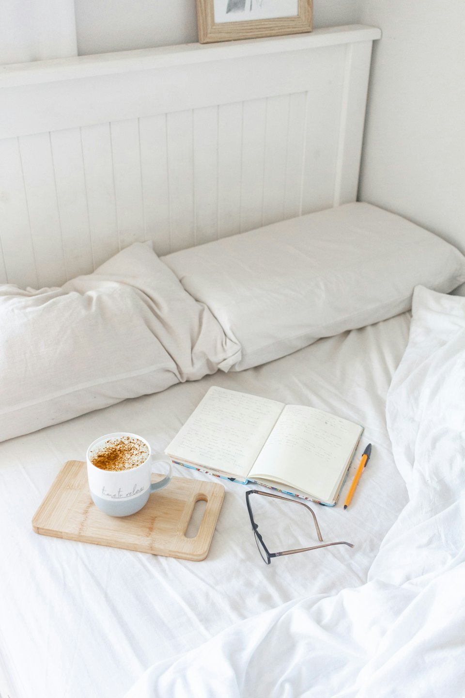 A mug of spiced drink, notebook, and glasses on white linens.