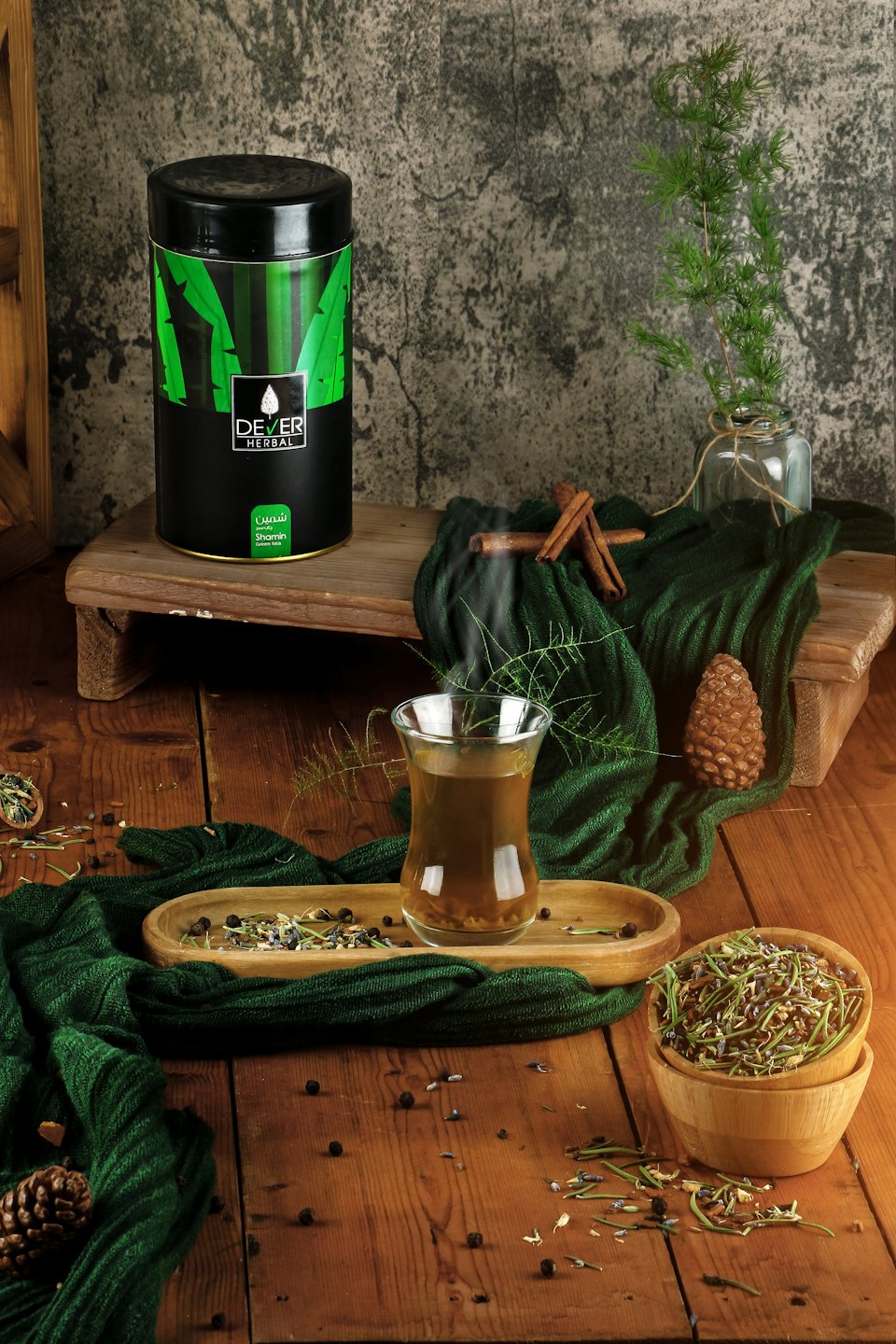 A tea canister and steaming glass sit among scattered herbs.