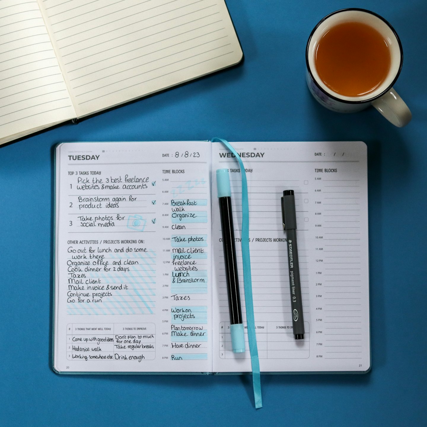Open planner with handwritten tasks and pens on a blue background.